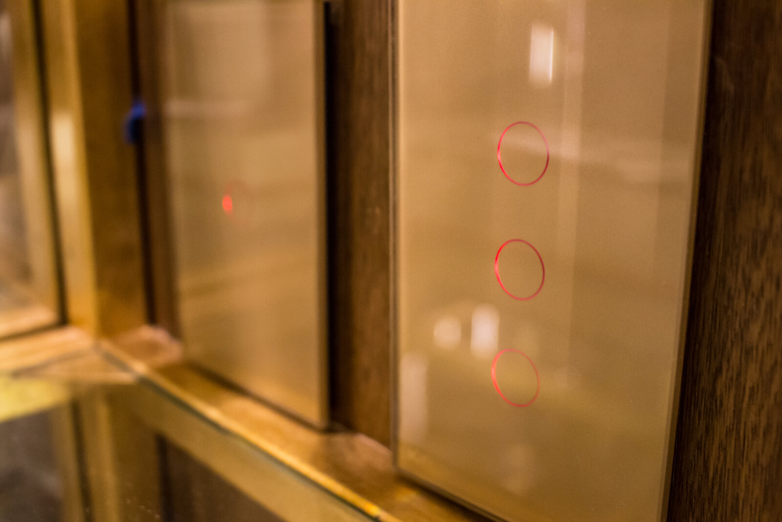 Interruptores ION Glass dorados instalados en panel de madera oscura — línea premium en acabado champagne