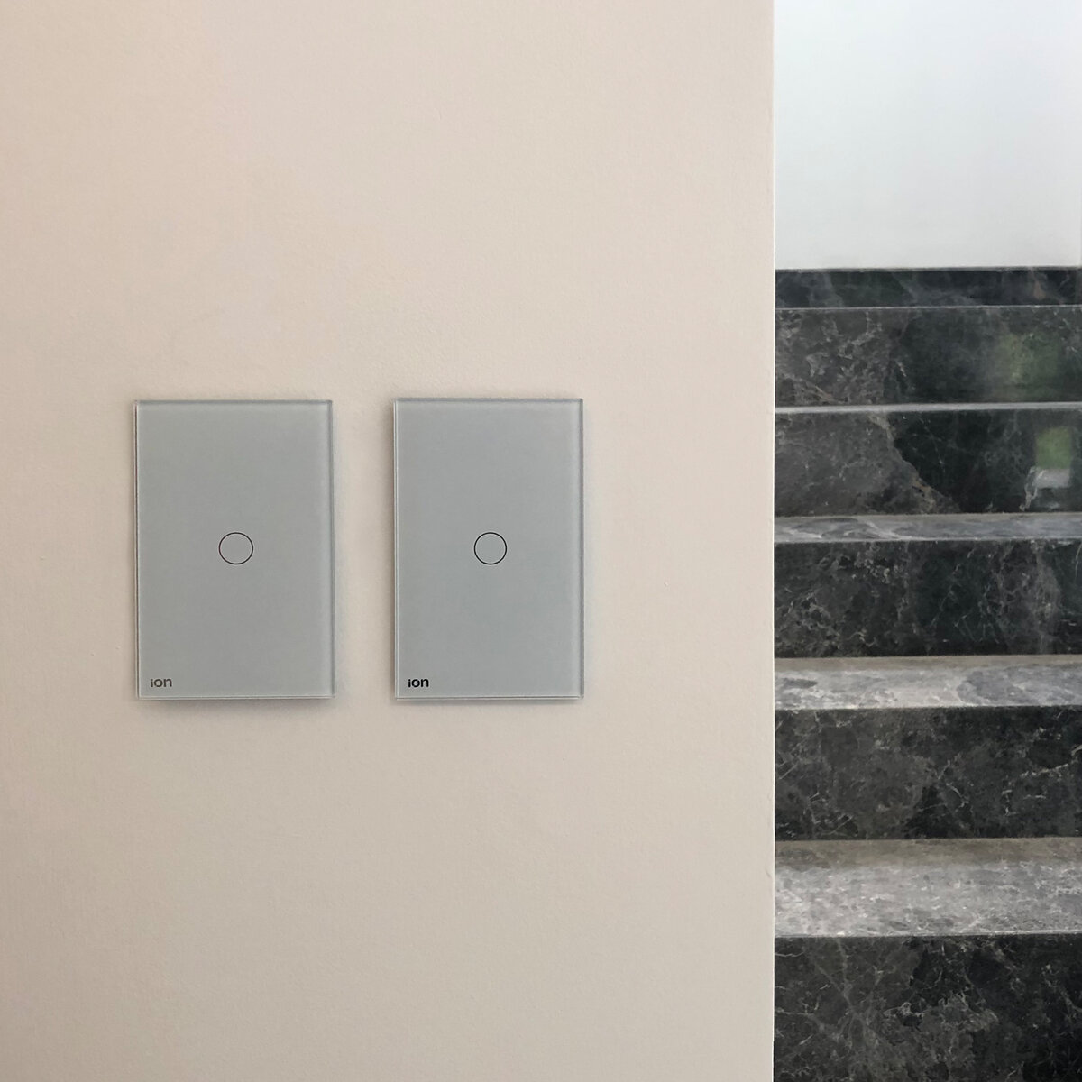 Interruptores ION Glass grises instalados en pared con escalera de mármol — ambiente residencial de lujo