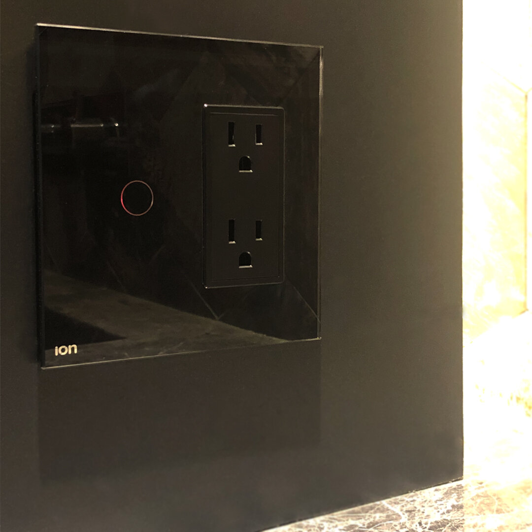 Módulo mixto ION Glass negro — interruptor touch y tomacorriente en panel de vidrio sobre mármol oscuro